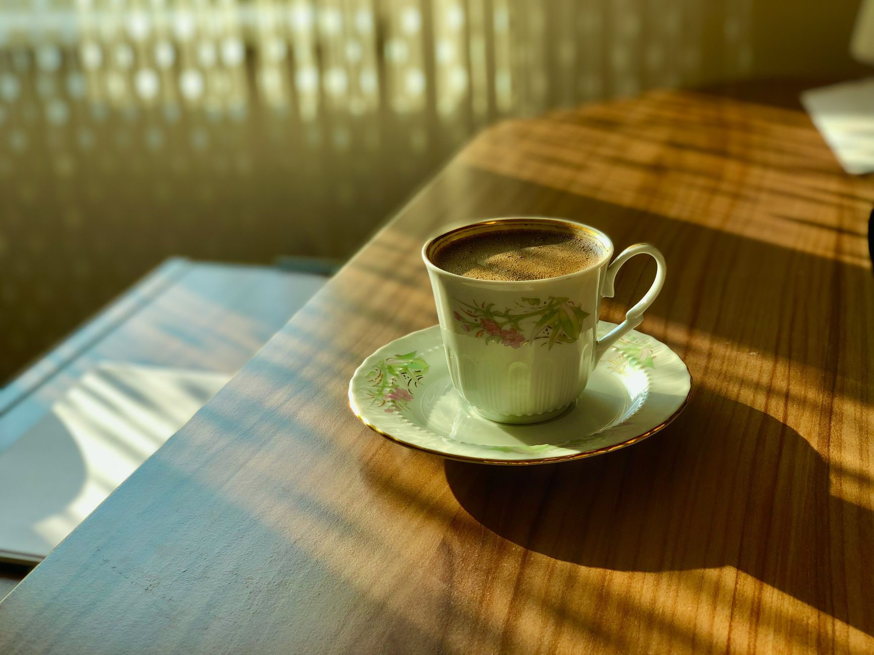 Elegant porcelain coffee cup catching sunlight on a wooden table, creating a calming morning scene.