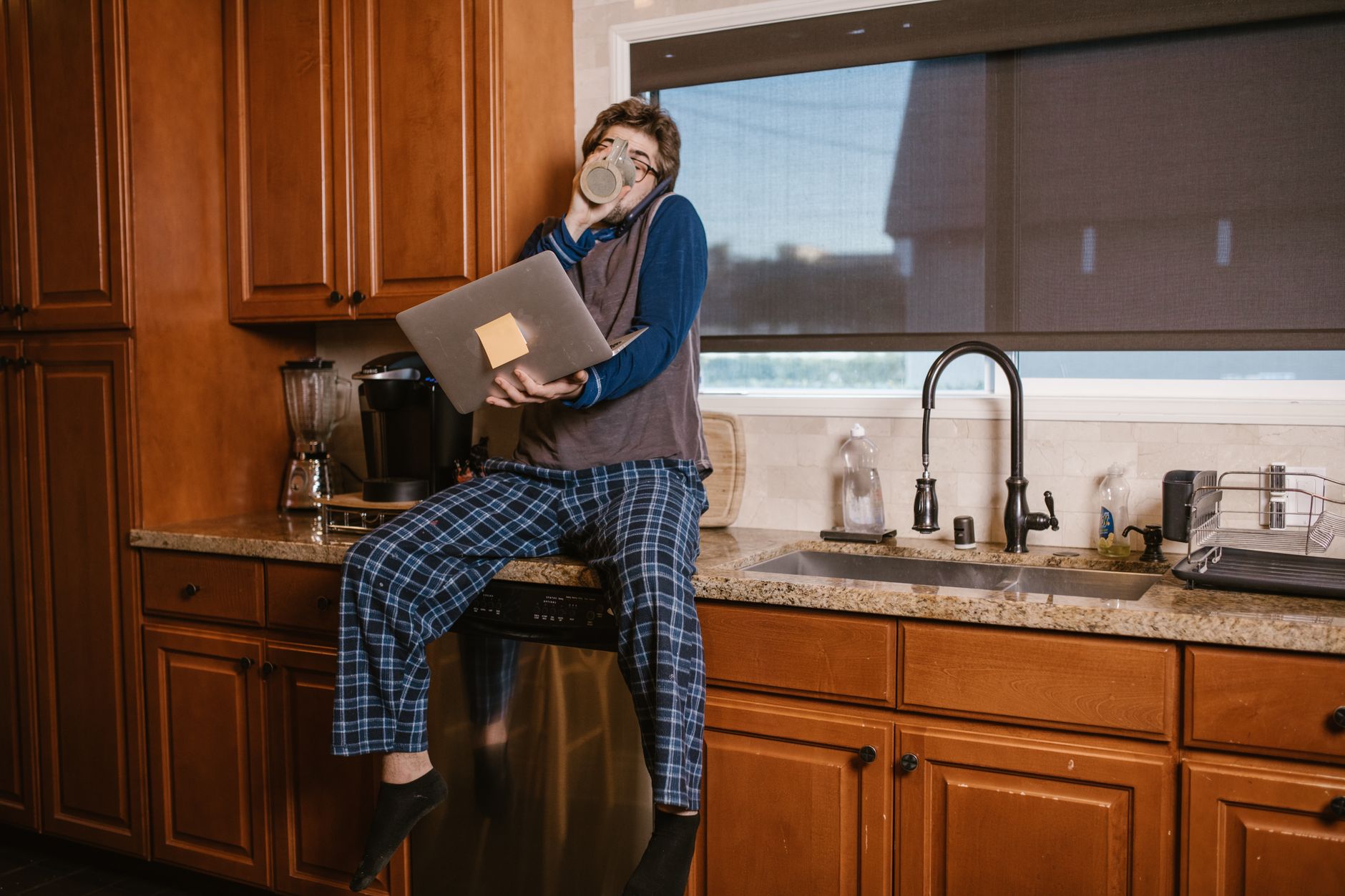 Person at kitchen counter with laptop and coffee in the early morning, relaxed home atmosphere.