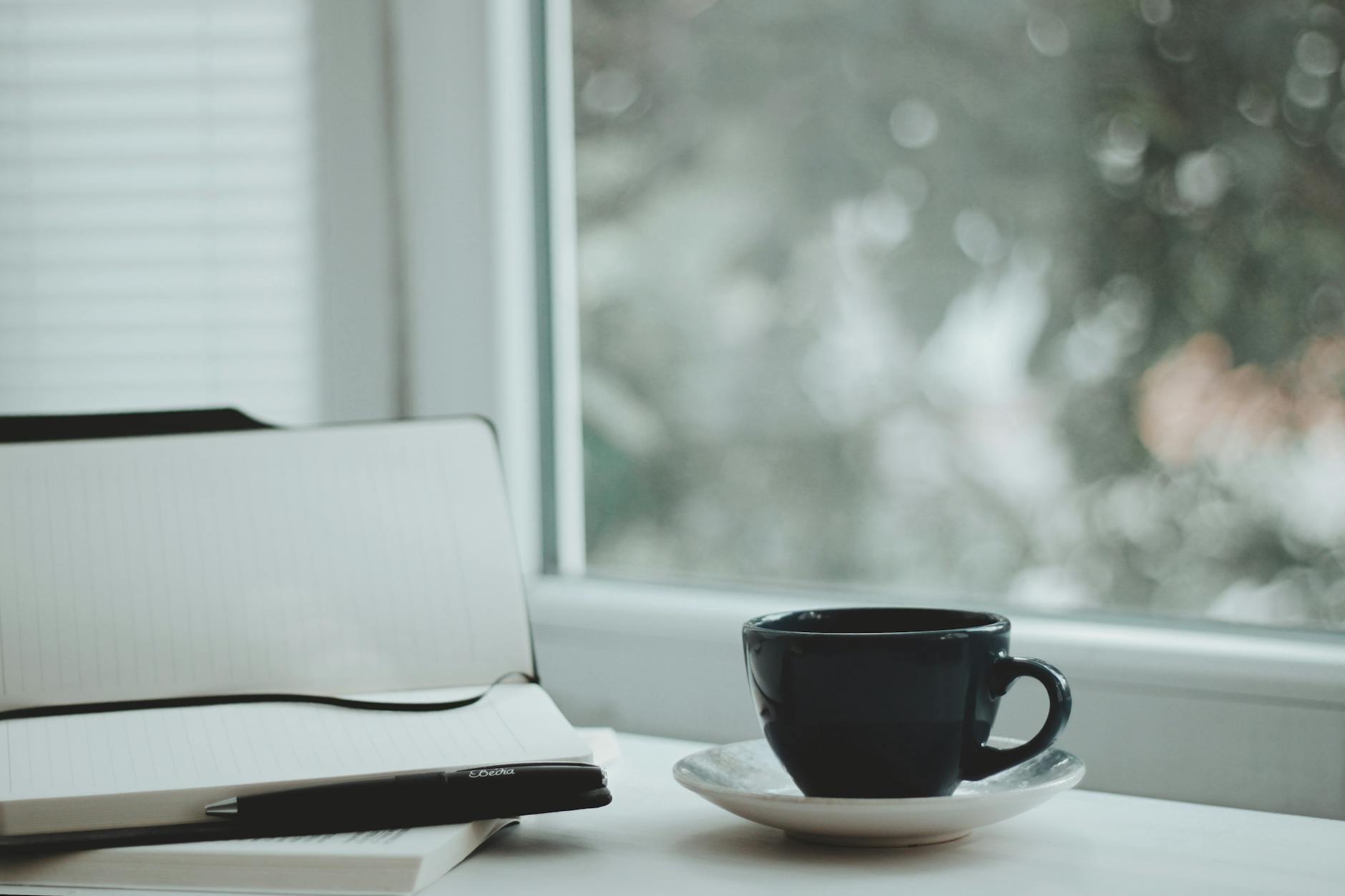 A serene scene with a coffee cup and notebook by a window, perfect for calm mornings.