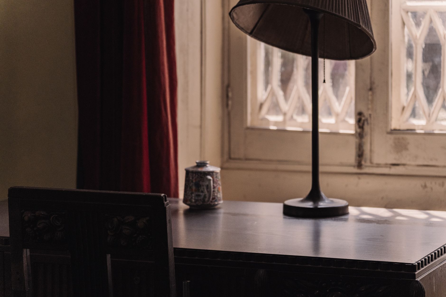 A rustic desk with a vintage lamp by a window casting soft natural light. Ideal for a cozy workspace.