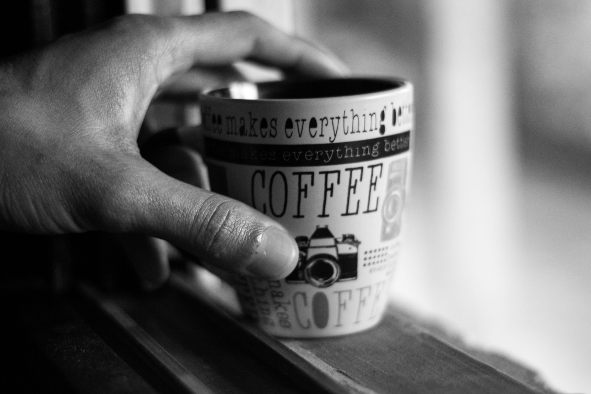 A black and white photo of a hand holding a coffee mug with inspirational text and camera design.