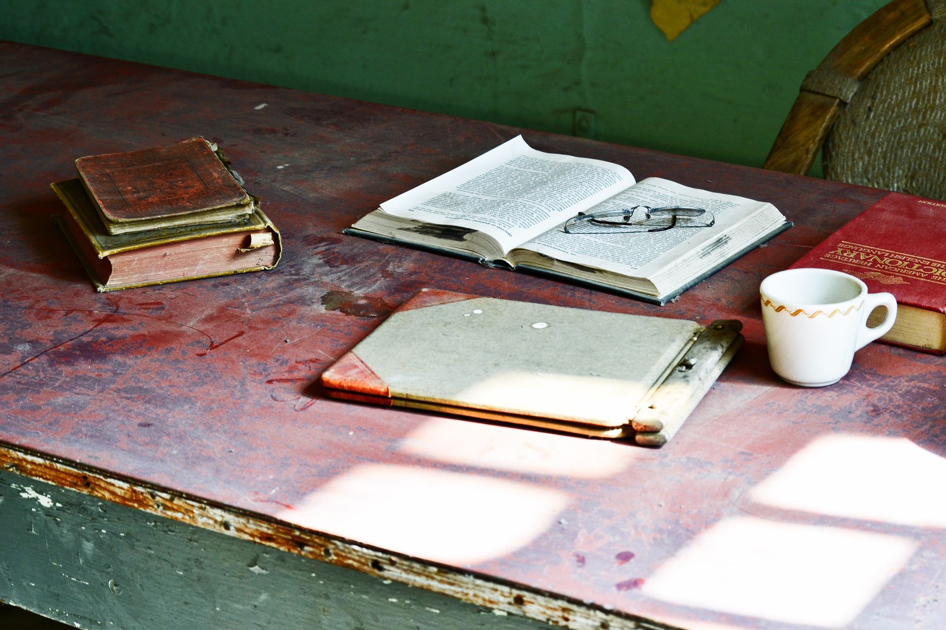A rustic wooden desk with antique books, open text, and a cup, bathed in soft sunlight.