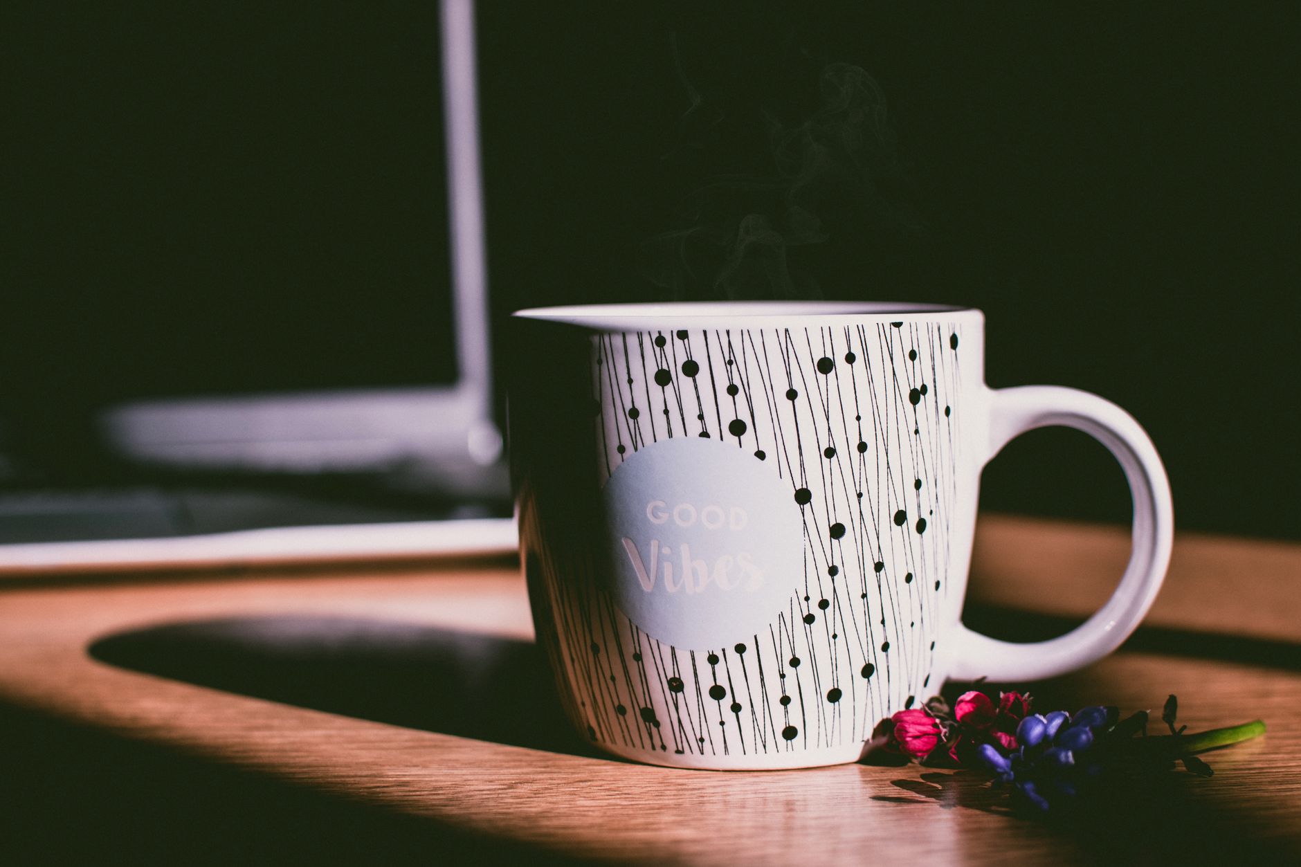 A ceramic mug on a wooden desk with flowers in the background.