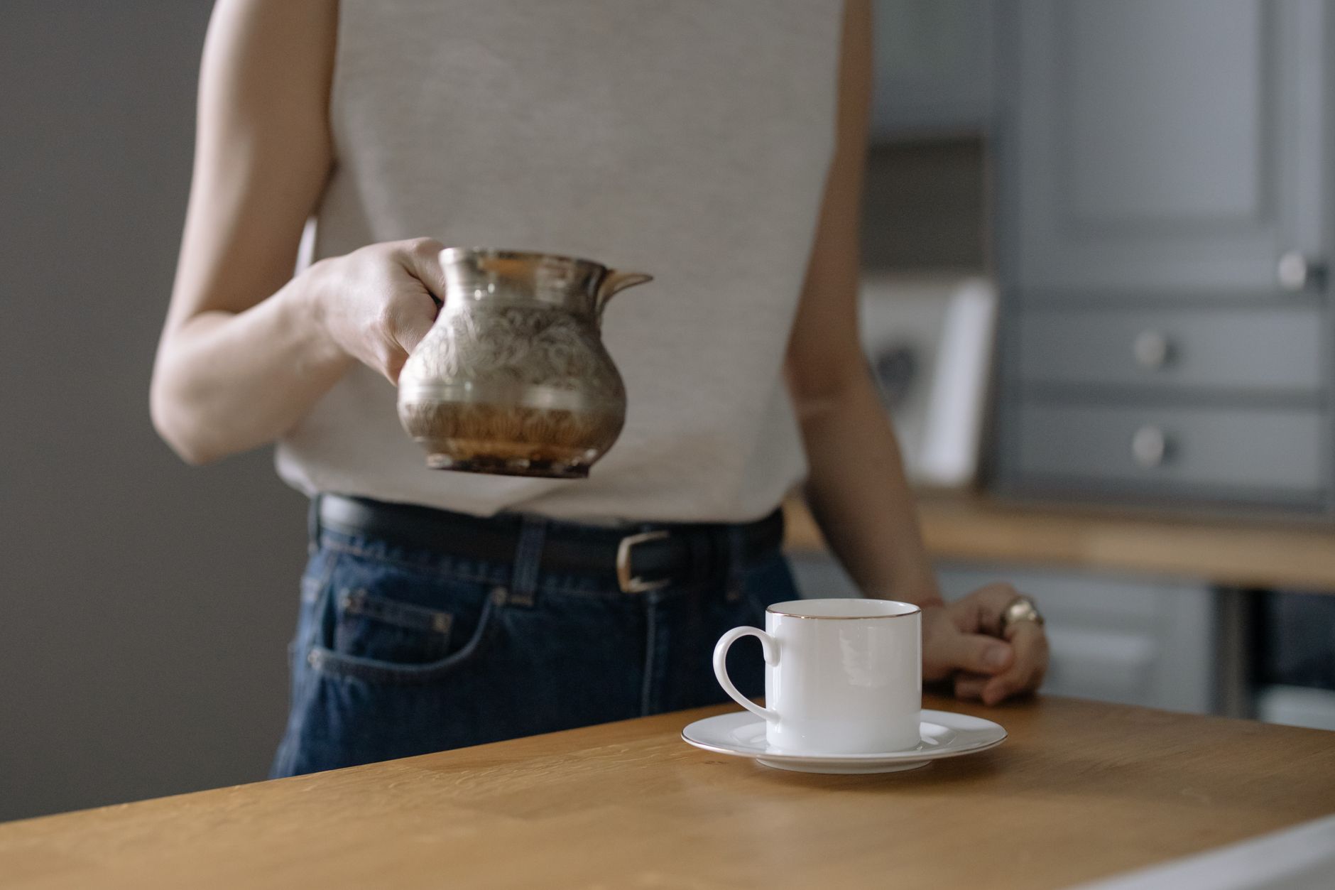 A person pouring coffee at a quiet kitchen table in the morning.