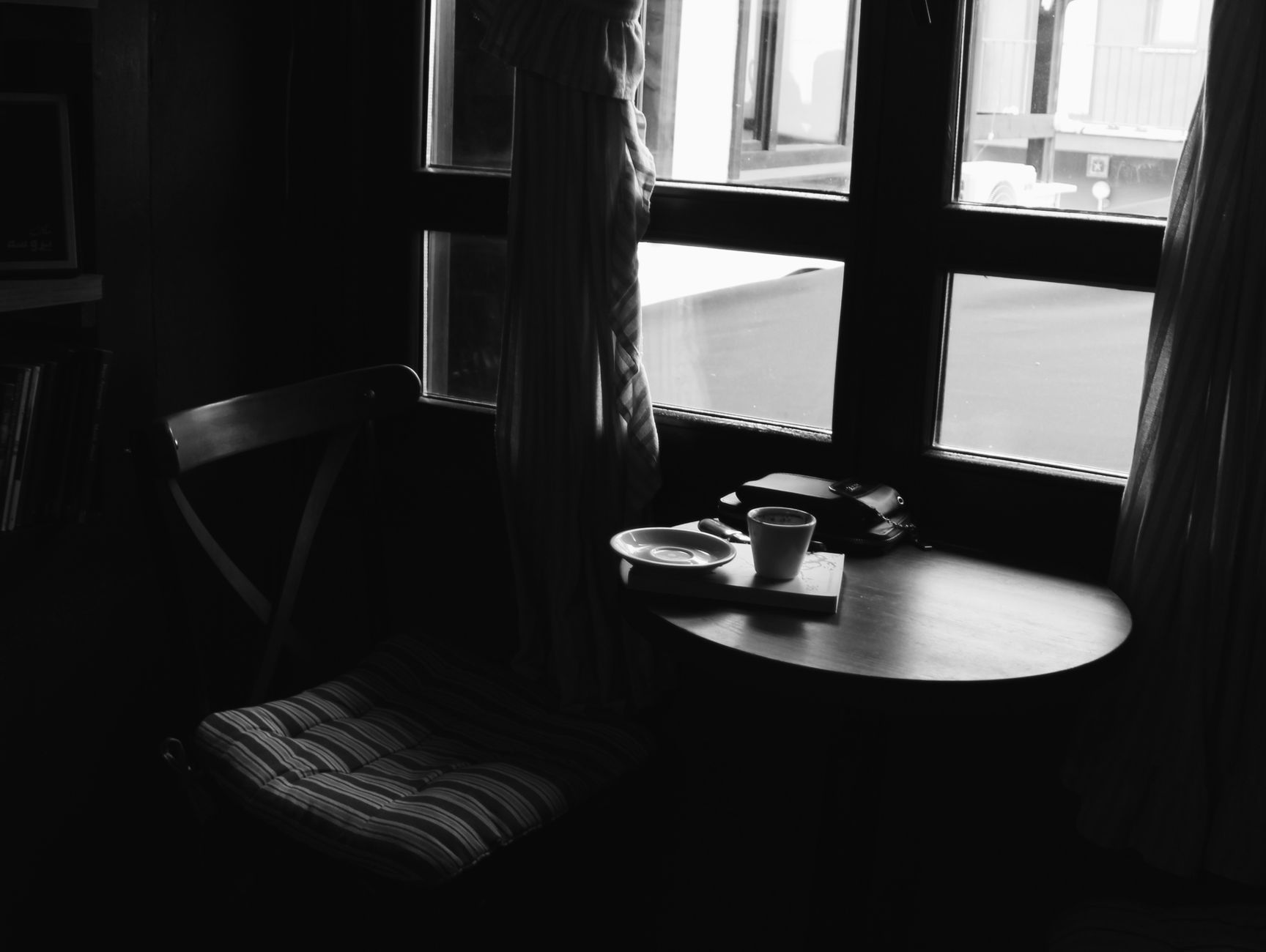 A black and white photo of a cozy cafe corner with a coffee cup on a table, evoking a moody atmosphere.