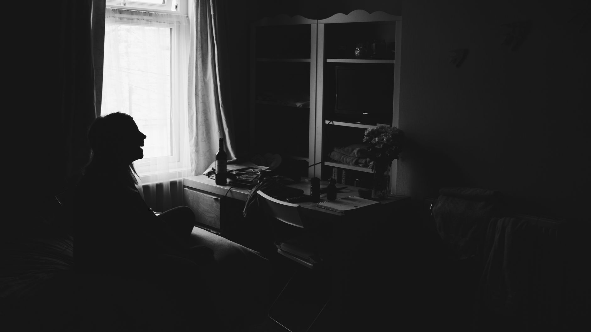 A silhouette of a woman sitting alone in a dimly lit room, capturing a mysterious mood.