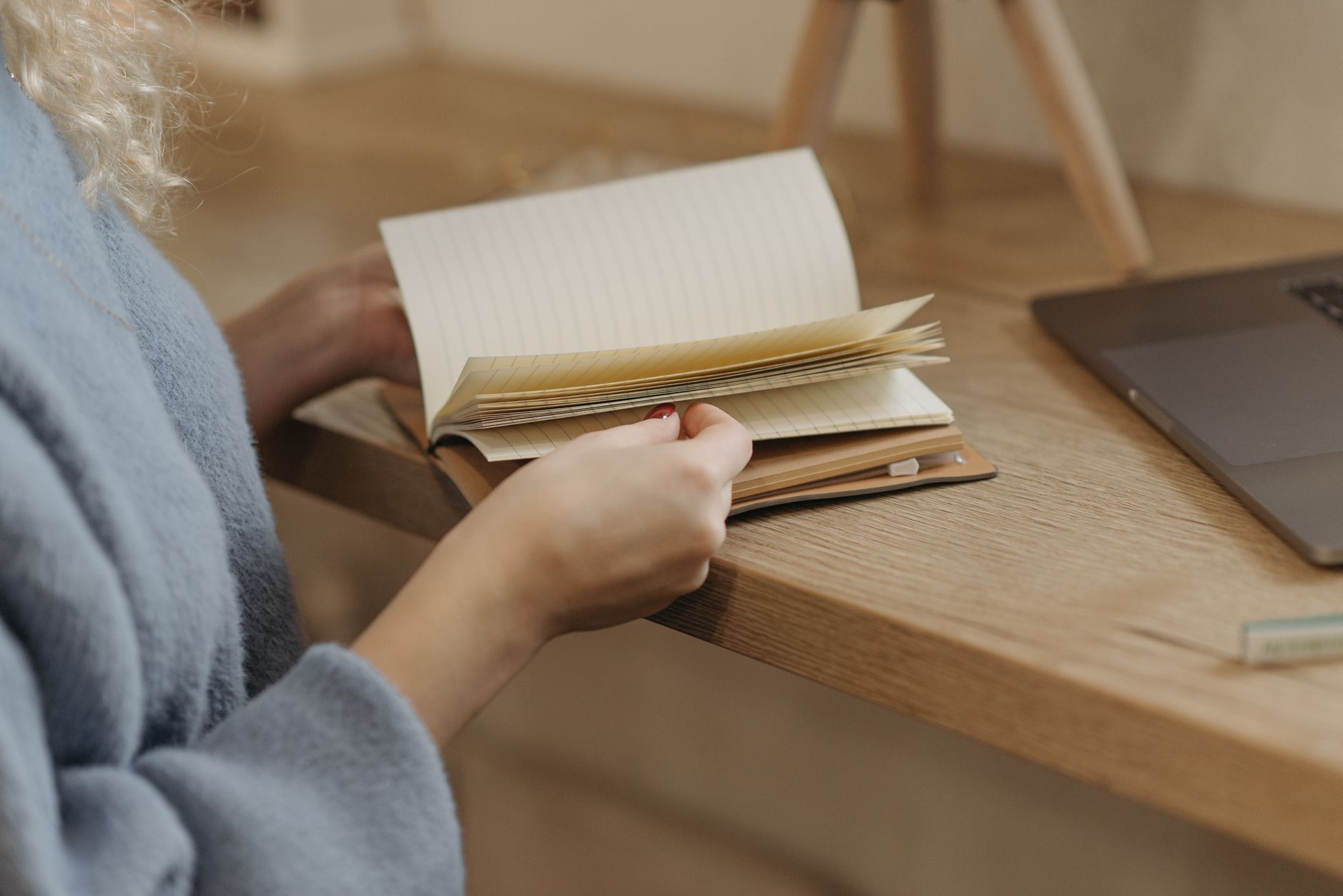 Person flipping through a notebook beside a laptop on a wooden table.