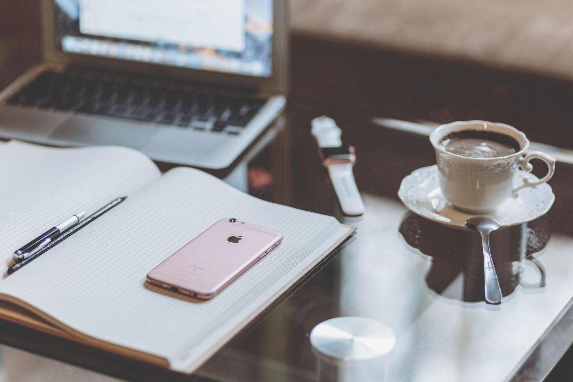 A comfortable desk setup with a laptop, smartphone, and coffee creating a cozy workspace atmosphere.