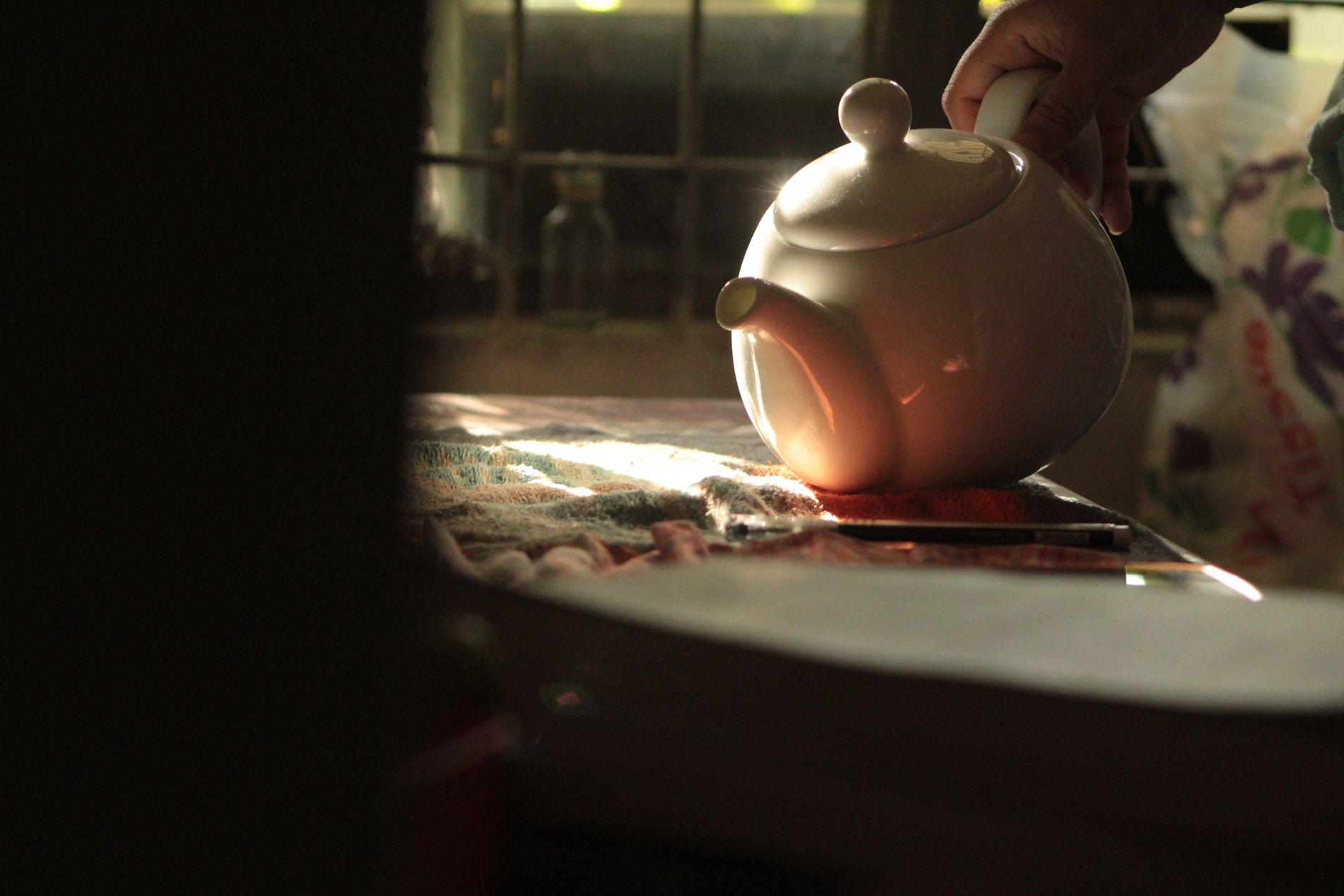 A warm sunlight illuminates a teapot on a table, evoking a cozy indoor ambiance.
