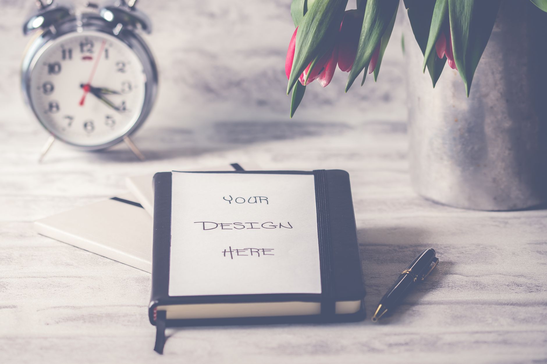 Stylish desk scene featuring tulips, a clock, and a notebook with customizable cover.