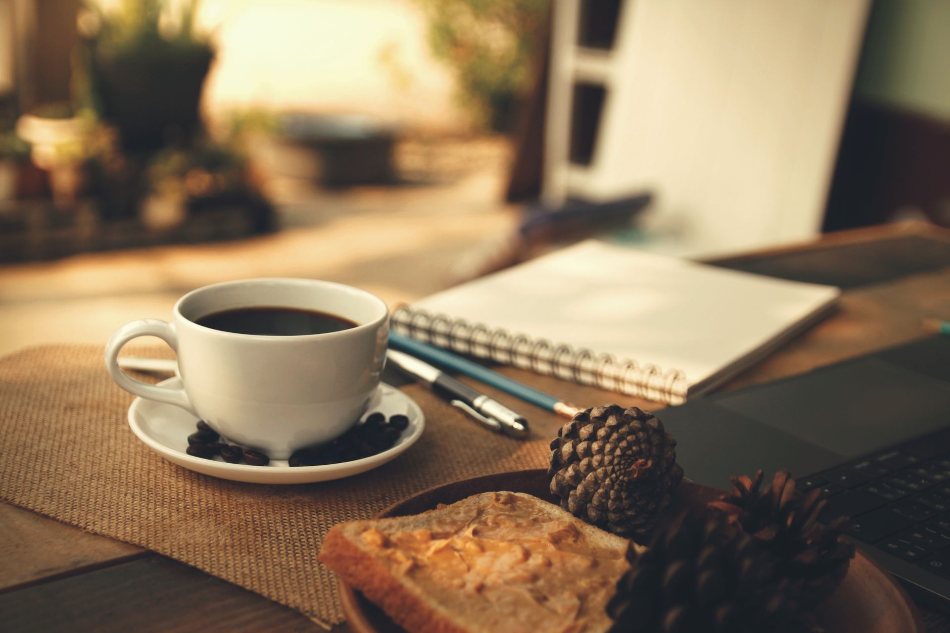 Warm morning workspace with coffee, notebook, and peanut butter toast.