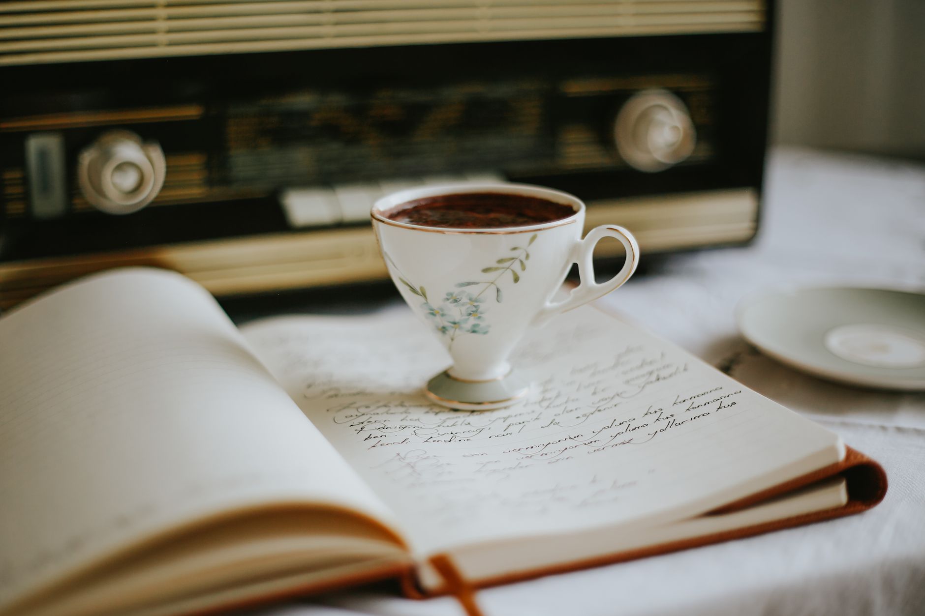 A vintage teacup on an open notebook with an old radio in the background, creating a nostalgic atmosphere.