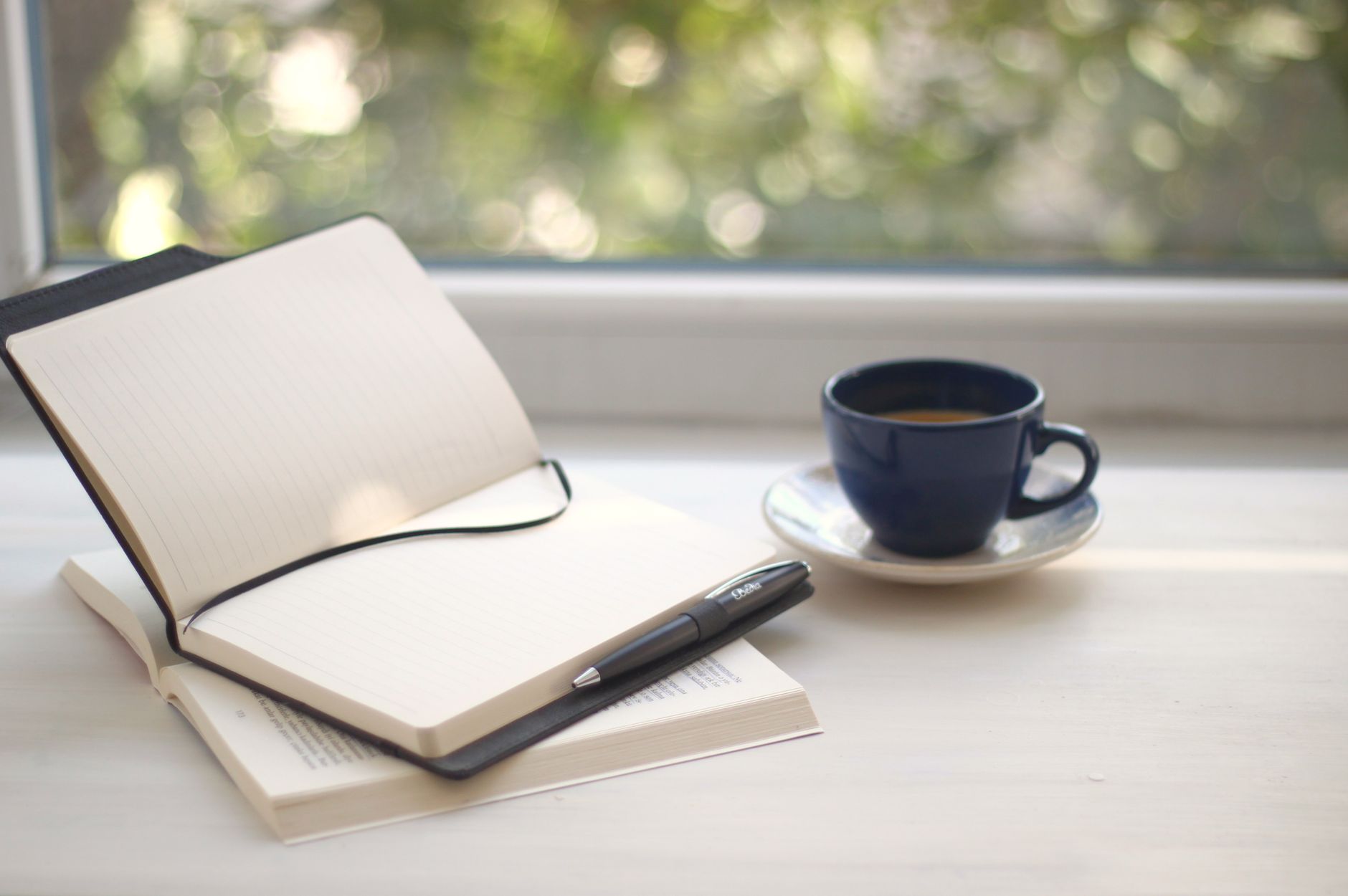 Cozy workspace setup with open notebook and coffee near a sunlit window.