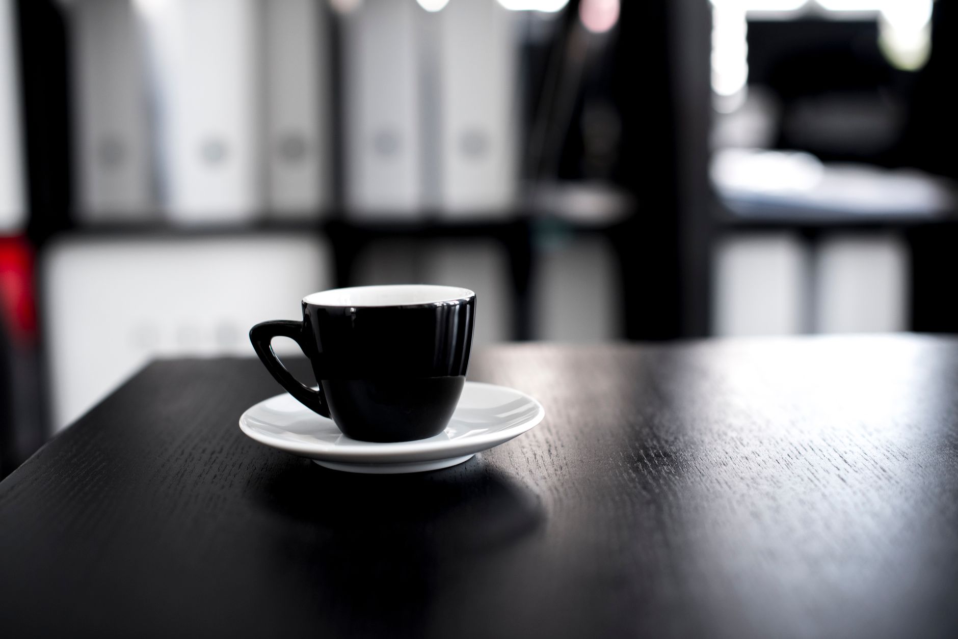 Black coffee cup on a wooden desk in an office setting. Minimalist and modern interior design vibe.