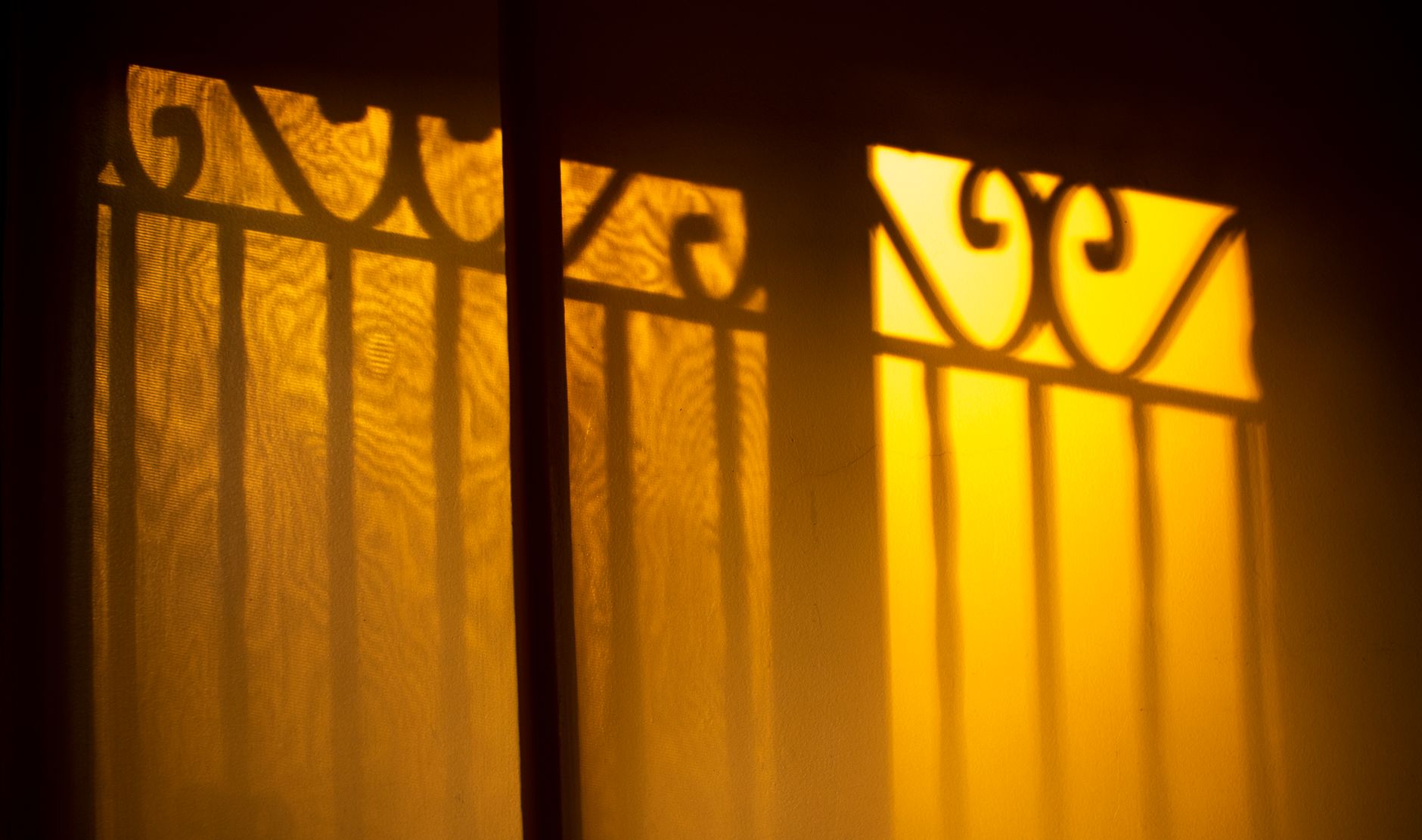 Silhouettes of ornate wrought iron casting shadows on a golden wall.