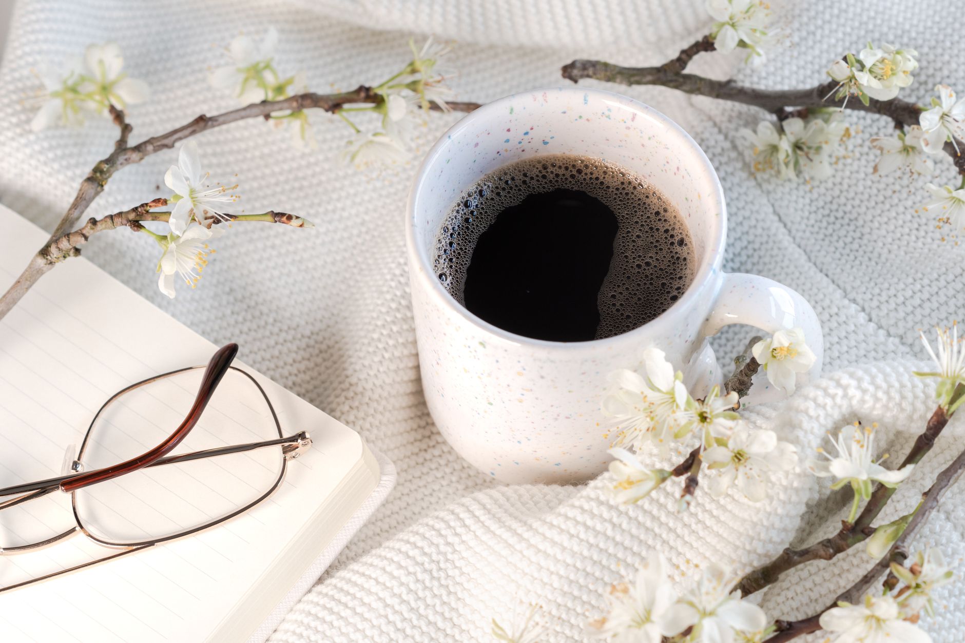 A serene cup of coffee surrounded by spring blossoms on a textured surface.