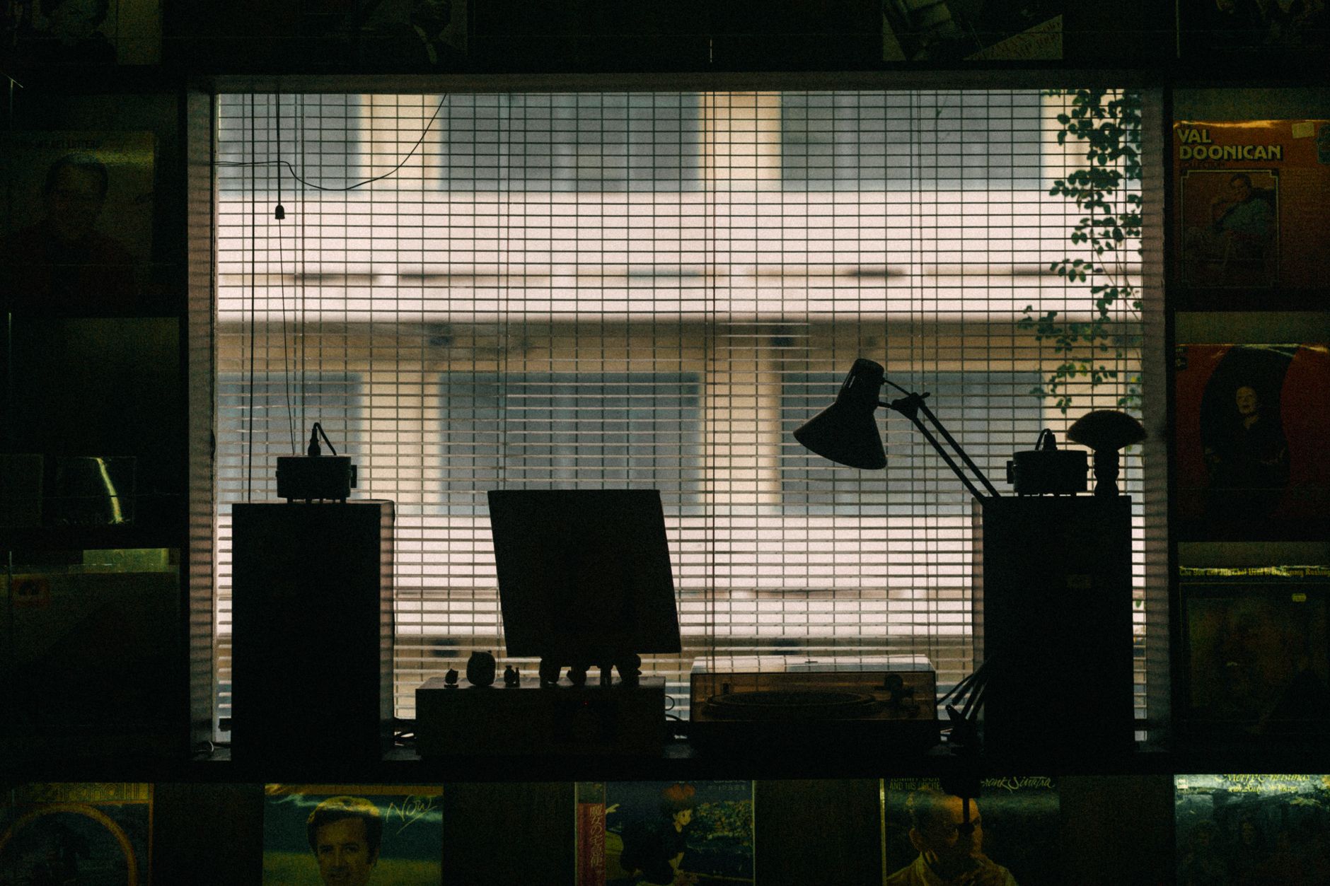 Silhouetted workspace with a vintage lamp and blinds, creating a moody indoor atmosphere.